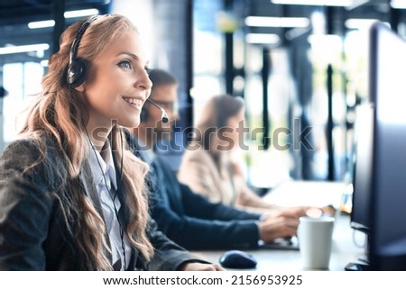 Female customer support operator with headset and smiling, with collegues at background. Royalty-Free Stock Photo #2156953925