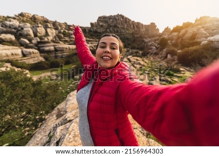 A beautiful shot of a Caucasian girl with red jacket smiling while taking a selfie with her camera in El Torcal de Antequera, Malaga, Spain