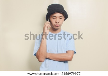 Portrait of sad asian young man wearing black hat carrying phone, isolated background
