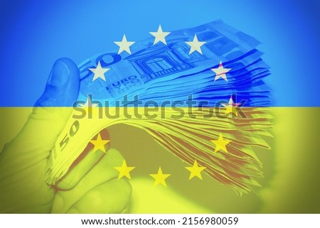 Hand holding european banknotes with the Ukrainian flag as background. Concept of Financial help from Europe. Royalty-Free Stock Photo #2156980059