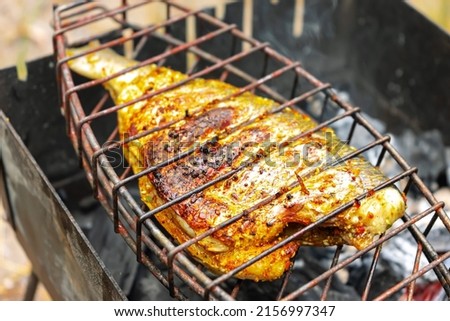 Grilled fish fried with lemon, citrus and spices, pepper. Exotic dietary marine fish. Dorado and perch in a restaurant recipe. Fish steak, barbecue, picnic. Fish cooked on fire coal on grill.