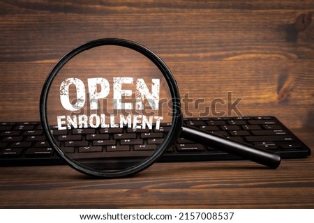 Open Enrollment. Search, Research and Registration concept. Magnifying glass and computer keyboard on a wooden background.