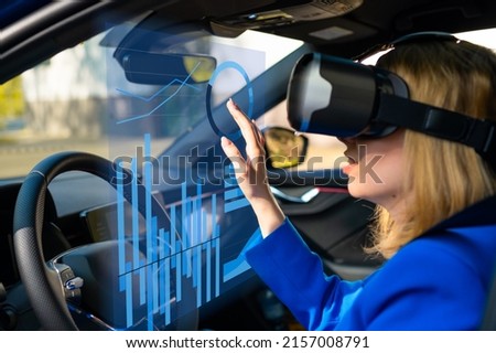 Digitally generated graphics and charts interface managed by business woman in vr googles sitting in the car in a blue suit. Metaverse cyber world technology concept. 