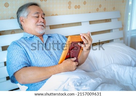 Mature man sad alone sick and lonely at home, Portrait Asian Senior man embracing picture frame with picture of a loved person,  life love and family insurance and health concept.
