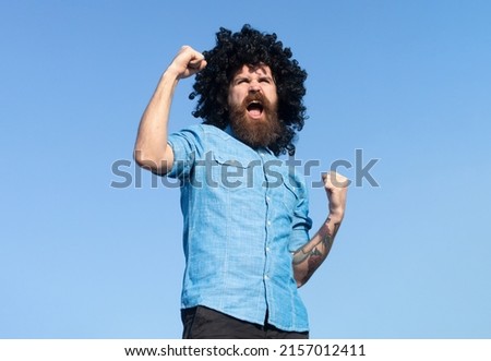 Funny nerdy guy. Crazy funny bearded man with wig on sky background. Expression and success.