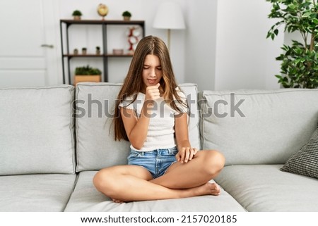 Young brunette teenager sitting on the sofa at home feeling unwell and coughing as symptom for cold or bronchitis. health care concept. 