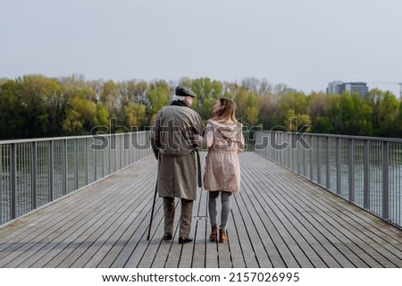 Rear view of senior man with daughter outdoors on a walk on pier by river. Royalty-Free Stock Photo #2157026995