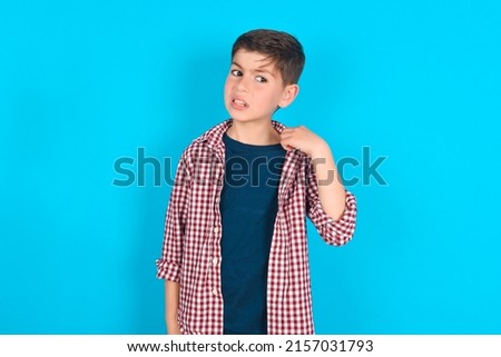 caucasian kid boy wearing plaid shirt over blue background stressed, anxious, tired and frustrated, pulling shirt neck, looking frustrated with problem