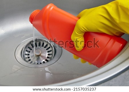Hand in yellow rubber glove pour sewer pipe cleaner down the kitchen sink drain. Kitchen and drain cleaning work Royalty-Free Stock Photo #2157035237