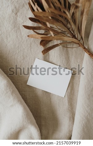 Blank paper sheet card with mockup copy space, dried protea flower on neutral beige linen blanket. Minimal aesthetic business brand template. Flat lay, top view