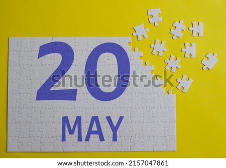 20 may calendar date on a white puzzle with separate details. Puzzle on a yellow background with blue inscription