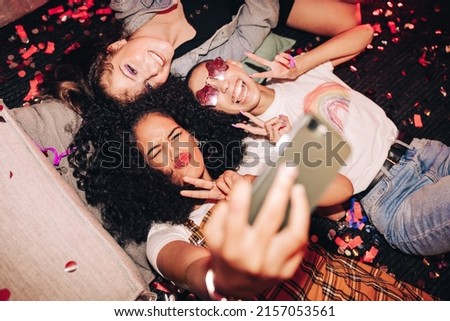 Capturing crazy party moments. Top view of three happy friends taking a selfie while lying on the floor at a house party. Group of cheerful female friends having fun together on the weekend.