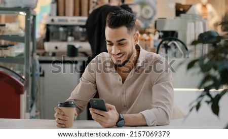 Indian hispanic arabian man multiracial businessman sitting at cafe table drinking hot coffee tea from paper cup looking in mobile phone typing smartphone chatting browsing using online app free wi-fi Royalty-Free Stock Photo #2157069379