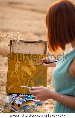 Back view of a girl painter depicting wheat spikelets on canvas. Young girl doing her favourite hobby Royalty-Free Stock Photo #2157077897