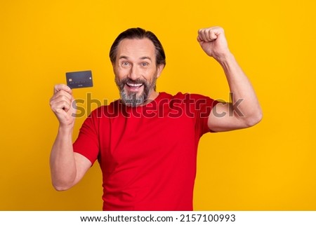 Photo of lucky funky retired man wear red t-shirt rising fist bank card isolated yellow color background