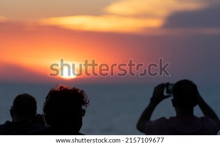 people photographing a sunset in the sea