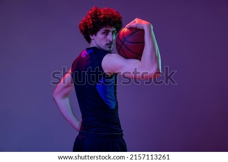 Back view of male muscular basketball player wearing blue sportswear isolated on purple background in neon. Concept of sport, movement, energy and dynamic, healthy lifestyle. Copy space for ad