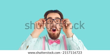 Wow, look at that. Headshot of funny surprised nerd. Geeky adult man wearing glasses, shirt and pink bow tie standing on turquoise studio background and looking at camera with amazed face expression