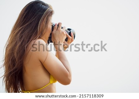 Young Asian woman shooting on digital camera.
Female photographer in yellow bikini holding dslr camera taking photos. tourist lifestyle travel hobby concept.