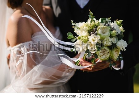 The bride and groom with a wedding bouquet, holding on hands and standing on wedding ceremony of the outdoor in the nature backyard.