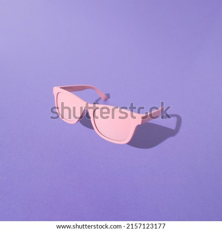 Pink sunglasses with sunlight shadow on purple background. Minimal summer vacation convcept.