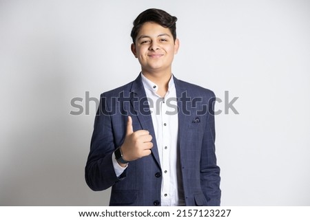 Portrait of a confident young indian teenager boy wearing suit do thumbs up isolated on white background.