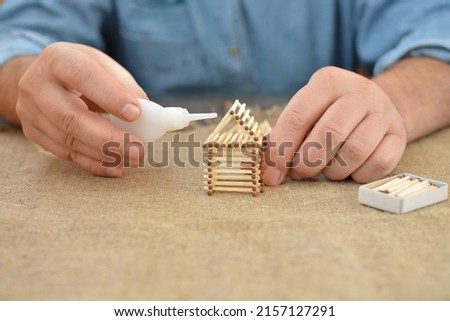 Old man engaged in manual work glue house with matches. Building dreams. Handmade. Blurring background. Free place. Needlework. Hobby. Construction. Concept. Royalty-Free Stock Photo #2157127291