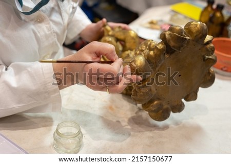 Experienced Lady Restoring a Small Gilded Statuette with a very Fine Brush in Her Art Studio.