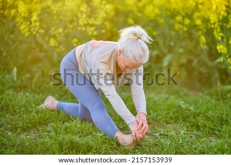 age woman relaxing on green grass during yoga exercise, morning routine, sunset light, outdoor. Mature female in sportswear doing stretching at nature open air. Age, healthy lifestyle.