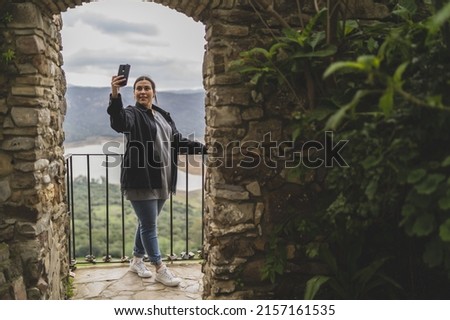 A photo of a Caucasian woman taking a selfie under the arc of a castle balcony