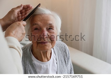 Unrecognizable female expressing care towards an elderly lady, brushing her hair with a comb. Granddaughter helping granny with a haircut. Family values concept. lose up, copy space, background. Royalty-Free Stock Photo #2157169751