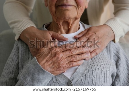Unrecognizable female expressing care towards an elderly lady, hugging her from behind holding hands. Two adult women of different age. Family values concept. lose up, copy space, background. Royalty-Free Stock Photo #2157169755