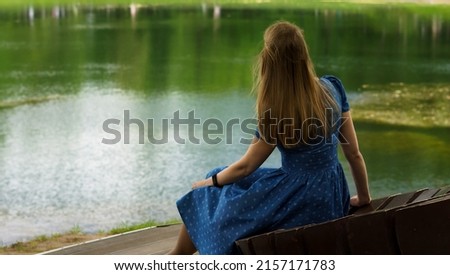 Young woman in blue dress sitting near the lake