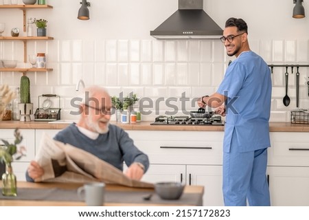 Cheerful caretaker preparing breakfast for an aged man Royalty-Free Stock Photo #2157172823