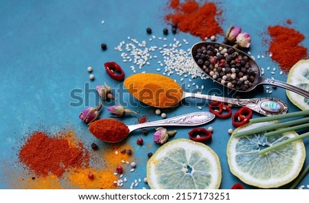 Still life with vintage silver spoons on a table. Aromatic spices and herbs on blue background. Natural antioxidants concept, Colorful picture of turmeric, paprika, chili pepper, sea salt, rose. 