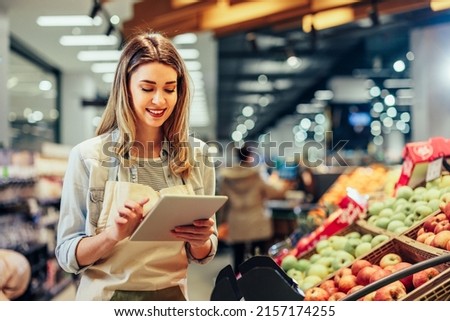 Young woman, employee with apron holding digital tablet and checking condition of product in the store Royalty-Free Stock Photo #2157174255