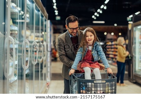 Dad is giving his daughter a ride in the shopping trolley while they're buying food in the supermarket Royalty-Free Stock Photo #2157175167