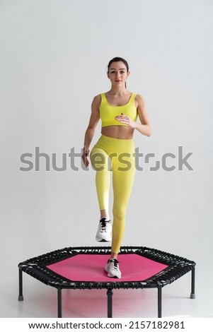 young fitness woman In sportswear jumping on sport trampoline White background Royalty-Free Stock Photo #2157182981