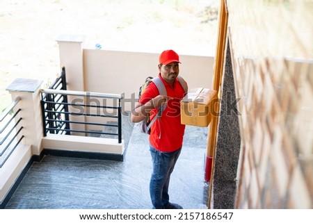 Delivery boy placing parcel in front of door after showing parcel to cctv or security camera - concept of security, safety and home courier service Royalty-Free Stock Photo #2157186547