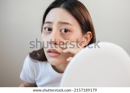 Sleepless Asian woman looking her face in the mirror and worry about dark circles under eyes