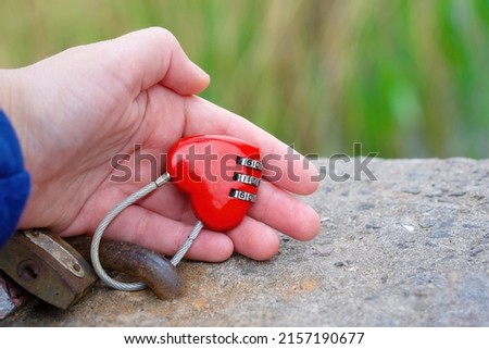 Hand holding a locked heart shaped love lock outdoors. Creative strong relationships concept.