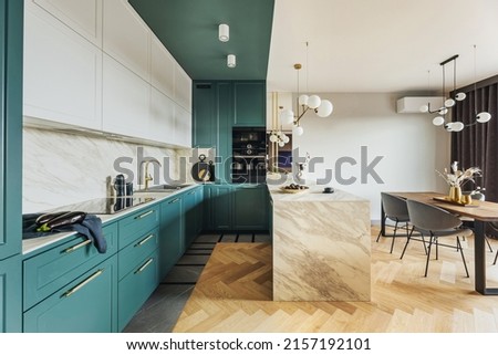 Luxury modern and vintage turquoise interior. Marble kitchen island with wooden chockers. Brown wooden table with metalic tray and metalic gold vase with white decorations.  Royalty-Free Stock Photo #2157192101