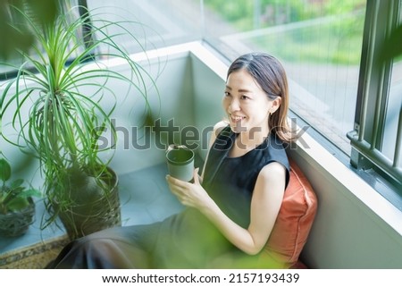 Asian woman relaxing surrounded by foliage plants Royalty-Free Stock Photo #2157193439