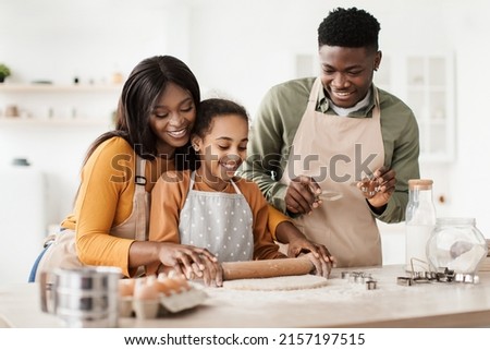 Cheerful Black Parents And Daughter Baking Pastry Rolling Out Dough For Cookies Spending Time Together In Modern Kitchen Indoor. Family Weekend Leisure And Food Recipes Concept