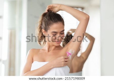 Young Lady Shaving Armpits Covered With Foam Removing Hair Standing Wrapped In Towel In Modern Bathroom. Woman Raising Arm Making Underarms Depilation. Hair Removal Concept Royalty-Free Stock Photo #2157198009