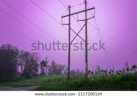 Electric pylons and power cables over the foggy forest at sunset with pink sky