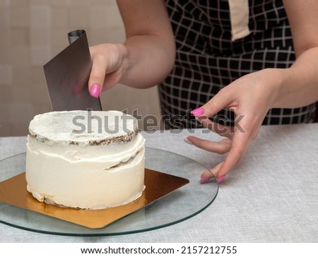 Women's hands using metal spatula align the cream on the sides of the cake. Selective focus. Picture for articles about food, cooking, confectioners.