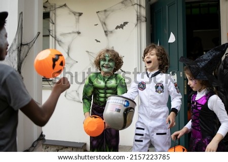 Group of trick-or-treating kids in face masks laughing on a porch of a house during Halloween