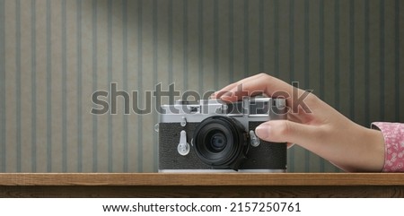 Woman holding a vintage camera and retro wallpaper in the background, creativity and hobbies concept