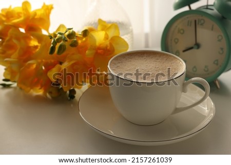 Morning coffee, alarm clock and flowers on white table indoors, space for text